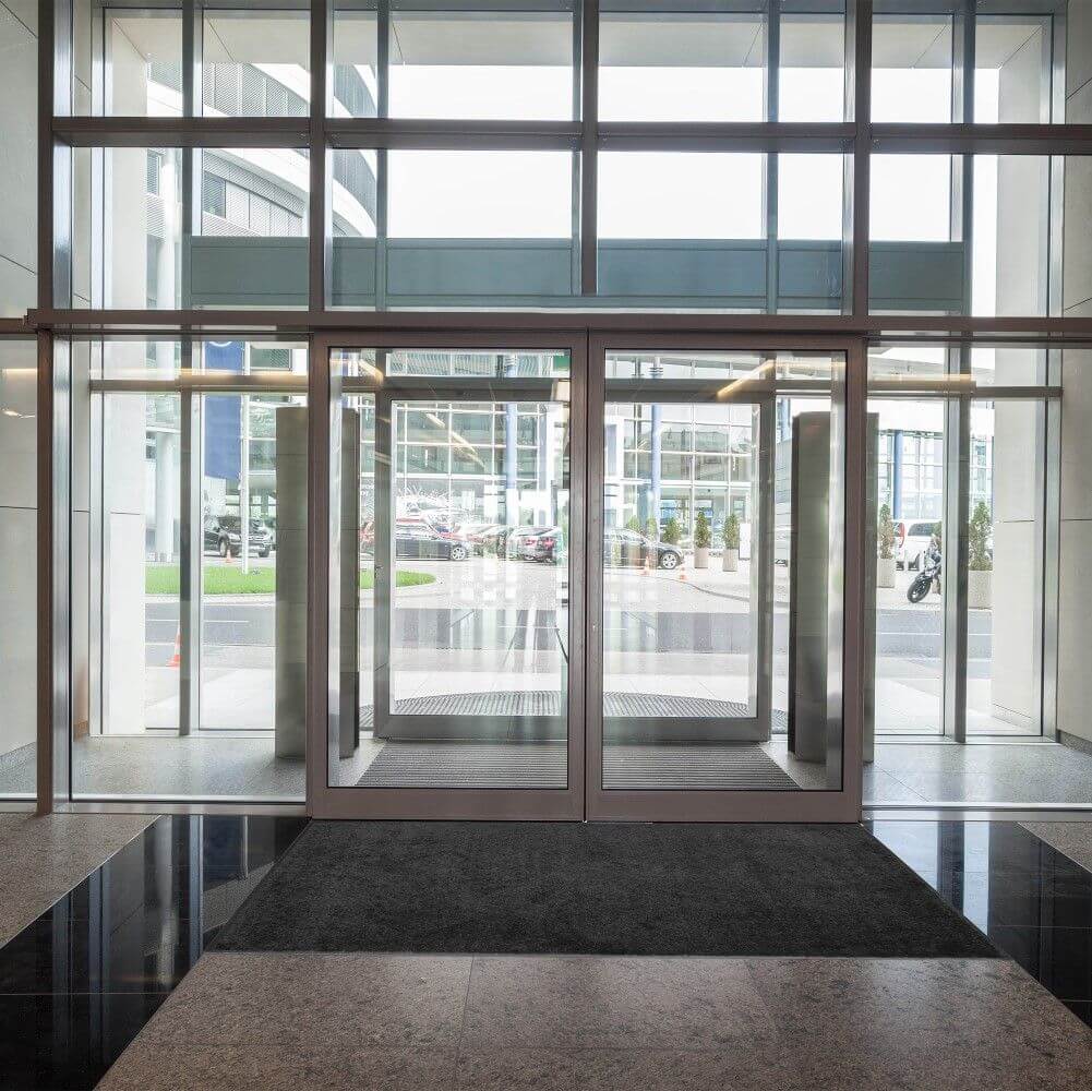 Looking out from inside a commercial building entry, noting the clean entrance mats that help prevent debris from entering the building, as well as slips and falls.